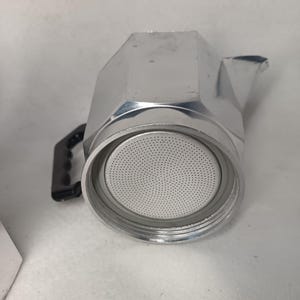 May include: A silver stovetop espresso maker with a black handle. The coffee pot is made of metal and has a round filter basket. The spout is on the right side of the pot. The coffee maker is designed to brew espresso.