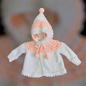 Knit baby sweater with hood and tie closure at neck.  White with peach accents.