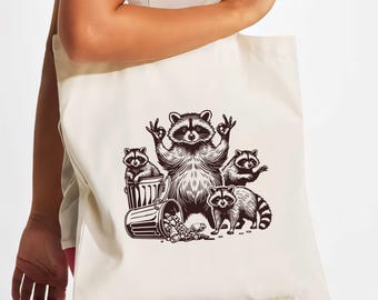 Könnte beinhalten: Eine weiße Canvas-Tragetasche mit einer Schwarzweiß-Illustration von vier Waschbären. Die Waschbären sitzen um einen Mülleimer herum, und einer von ihnen hält ein Peace-Zeichen. Der Text "Trash Pandas" ist auf die Tasche gedruckt.