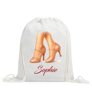 May include: A white drawstring bag featuring a graphic illustration of two legs wearing tan-colored high-heeled Mary Jane shoes with double straps. Below the illustration, the name Sophie is printed in a dark red, cursive script font.