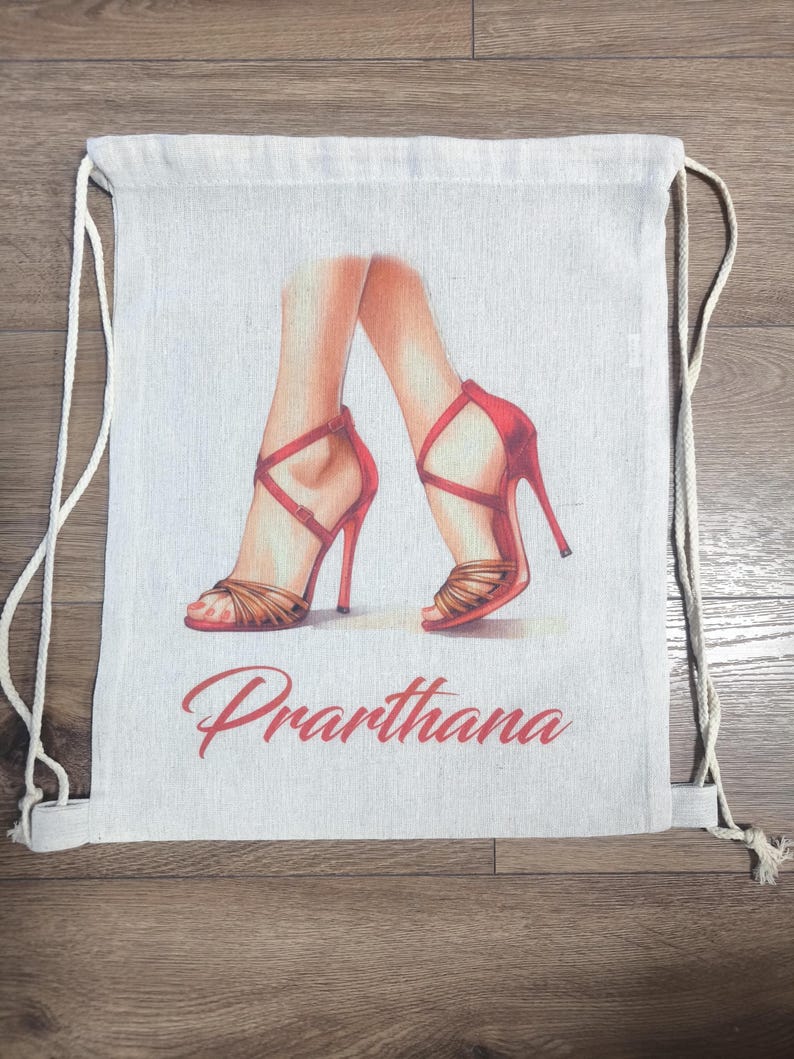 May include: A beige drawstring backpack featuring a printed illustration of two legs wearing red high-heeled sandals with crisscross straps. The name Prarthana is printed in red cursive script below the illustration of the footwear.