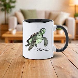Può includere: Tazza in ceramica bianca con interno e manico neri. La tazza presenta un'illustrazione dettagliata di una tartaruga marina nei toni del verde e del marrone, con il nome "Melania" in corsivo.
