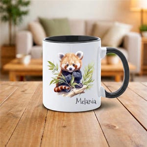 Peut inclure: Mug en céramique blanche avec intérieur et anse noirs. Il présente une illustration à l'aquarelle d'un panda roux sur une branche avec des feuilles vertes. Le nom "Melania" est imprimé en dessous.