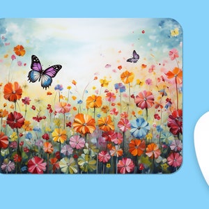Puede incluir: Una alfombrilla de ratón rectangular con una vibrante ilustración pictórica de un campo de flores silvestres coloridas en tonos naranja, rojo, rosa, amarillo y azul. Dos mariposas aparecen volando sobre las flores contra un cielo suave.