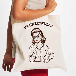 Può includere: Borsa tote color crema con un'illustrazione retrò di una donna con occhiali, rossetto rosso e una camicia bianca, che mostra il dito medio. La parola "RESPECTFULLY" è stampata sopra l'illustrazione in grassetto, marrone scuro.