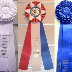May include: Three blue, red, and white ribbon rosettes with text that reads "San Diego County Fair", "LA County Fair", and "Philadelphia International Flower Show". The blue rosette has a blue tag that reads "First Place" and the red, white, and blue rosette has a gold tag that reads "Special Award".