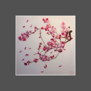 May include: Embroidered artwork featuring a branch of pink cherry blossoms with falling petals. The blossoms are detailed with varying shades of pink and white, set against a light background. The artwork is framed in white.