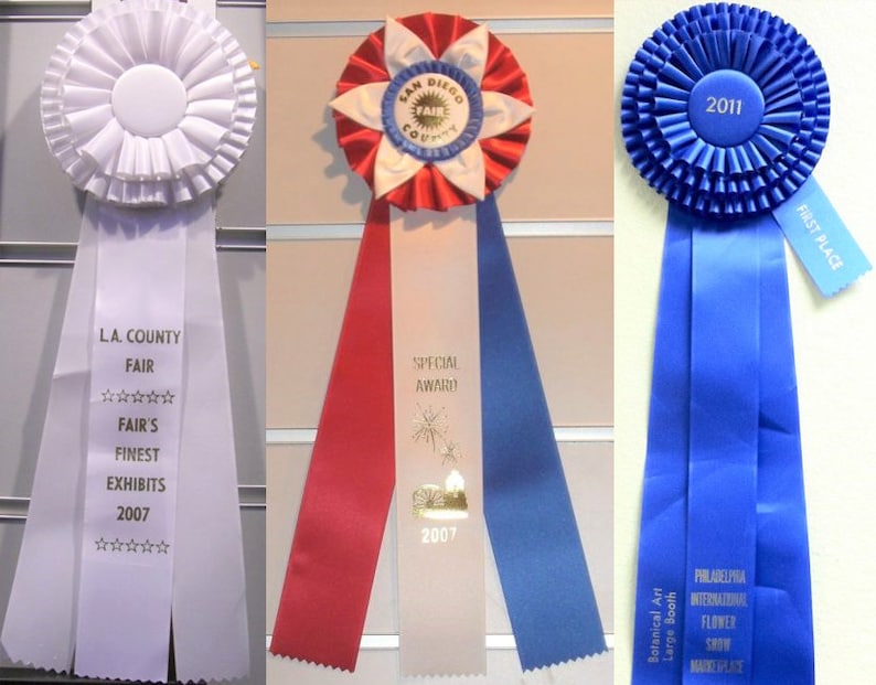 May include: Three award ribbons. The first is white with text "L.A. County Fair" and "Fair's Finest Exhibits 2007". The second is red, white, and blue with "San Diego County Fair" and "Special Award 2007". The third is blue with "First Place" and "2011".