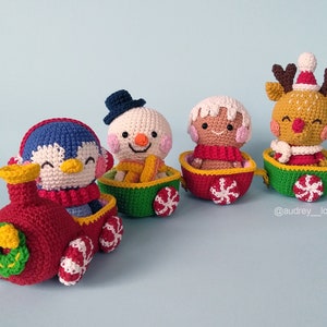 Puede incluir: Un tren de juguete de crochet con un pingüino, un muñeco de nieve, una persona de jengibre y un reno. El tren está decorado con bastones de caramelo y una corona.
