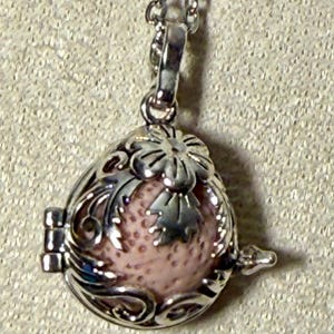 May include: Silver-toned pendant necklace featuring a teardrop-shaped locket with intricate floral filigree. The locket contains a pink, speckled stone. The pendant hangs from a delicate chain, creating an elegant accessory.
