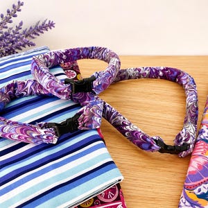 May include: Two circular fabric collars featuring a marbled pattern in shades of purple, blue, and white. Each collar is constructed from gathered fabric and includes a small black plastic side-release buckle for fastening and adjustment.