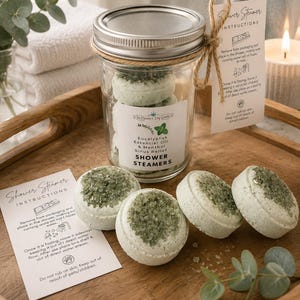 May include: A clear glass mason jar filled with round, pale green shower steamers topped with dark green crystals. The label reads Eucalyptus Essential Oil & Menthol Sinus Relief SHOWER STEAMERS. Includes two instruction cards and eucalyptus sprigs.