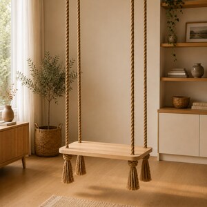May include: A rectangular light-toned wooden swing seat suspended by four thick, natural-coloured twisted jute ropes. Each rope features a decorative knotted tassel hanging below the seat, providing a stable and functional hanging platform.