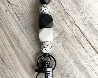 May include: Black and white silicone bead keychain with a piano key charm. The beads feature musical notes and a geometric design.