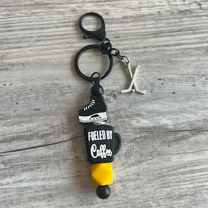 Peut inclure: Porte-clés noir et jaune avec un patin de hockey, une tasse à café avec le texte "Fueled by Coffee" et un charme de bâton de hockey.