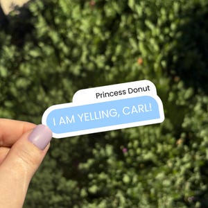 Może przedstawiać: Naklejka z napisem "I AM YELLING, CARL!" w niebieskim dymku, nad nim napis "Princess Donut". Naklejka jest trzymana na tle zielonych liści.