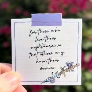 May include: A white square sticker with a purple border and a purple tape at the top. The sticker has handwritten text that reads "for those who live their nightmares so that others may have their dreams." A decorative sword and butterfly are at the bottom.