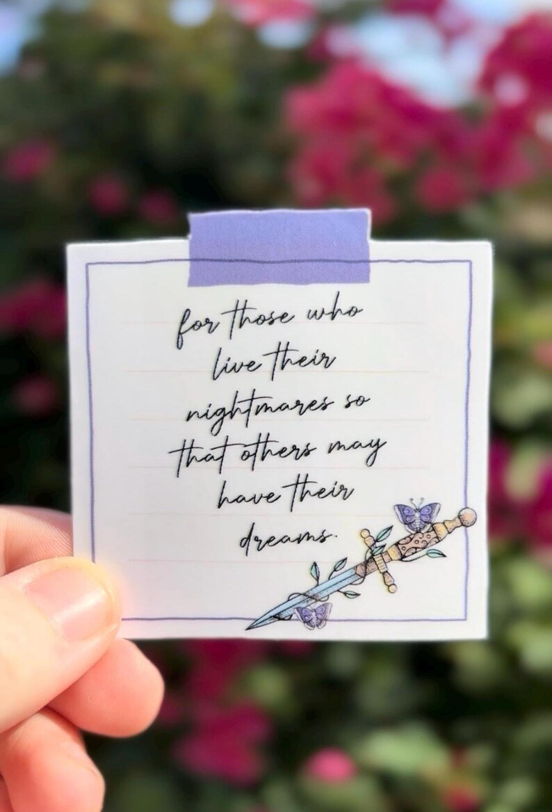 May include: A white square sticker with a purple border and a purple tape at the top. The sticker has handwritten text that reads "for those who live their nightmares so that others may have their dreams." A decorative sword and butterfly are at the bottom.