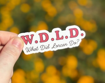 May include: A white sticker with the text "W.D.L.D. What Did Lorcan Do?" in a red, rounded font. The sticker is held against a blurred background of yellow flowers.