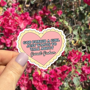 May include: A heart-shaped sticker with a pink center and a yellow scalloped border. The sticker features the text "GOD FORBID A GIRL JUST WANTS TO TALK ABOUT Garrett Graham" in a mix of fonts.