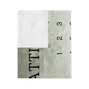 Pu&ograve; includere: Una morbida coperta bianca e verde con la scritta "ATTI" stampata in nero. La coperta ha un design simile all'acquerello con i numeri 1, 2 e 3. La coperta &egrave; piegata, rivelando un interno bianco.