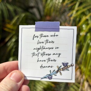 May include: A white sticker with a purple tape strip at the top. The sticker has a handwritten quote: "for those who live their nightmares so that others may have their dreams." A decorative sword and butterfly graphic is on the bottom right.