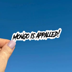May include: A white sticker with the phrase "MONGO IS APPALLED!" in black, stylized, brush-stroke lettering. The sticker is held against a bright blue sky background.