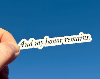 Pode incluir: Um autocolante branco com o texto "And my honor remains." contra um céu azul brilhante. O autocolante tem uma borda branca e o texto está numa fonte simples e elegante.