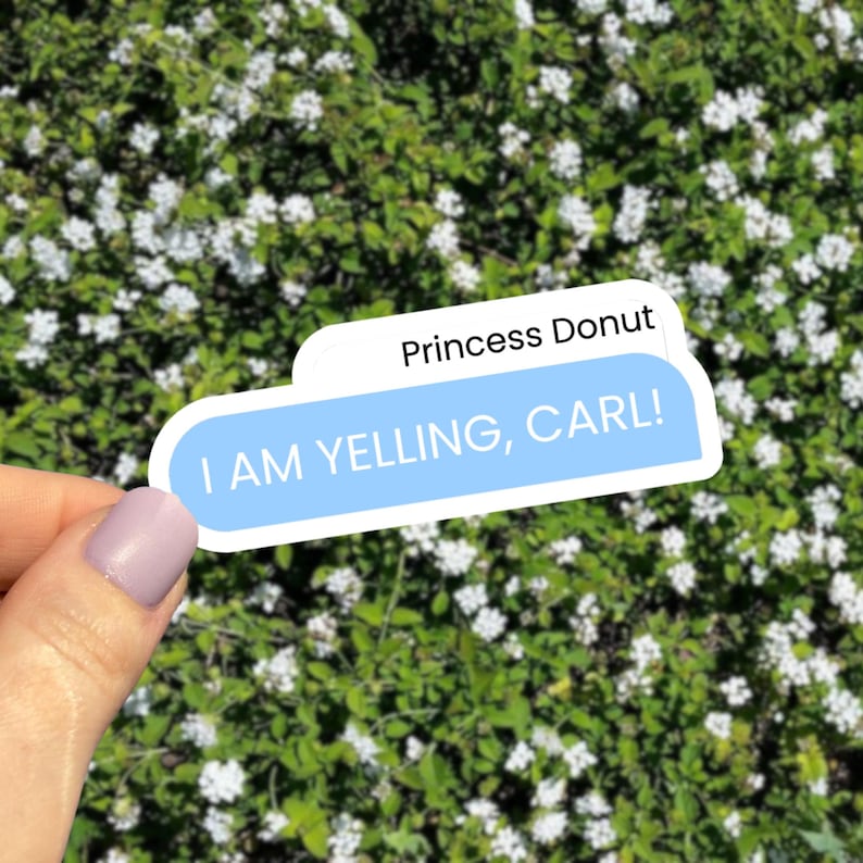 Puede incluir: Una pegatina con el texto "I AM YELLING, CARL!" en blanco sobre un fondo azul claro. La pegatina tambi&eacute;n tiene el texto "Princess Donut" en blanco sobre un fondo blanco. La pegatina se sostiene frente a un fondo de follaje verde con flores blancas.