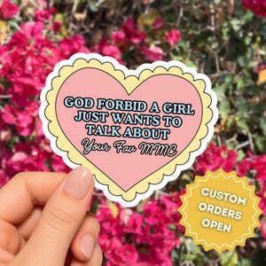 May include: A heart-shaped sticker with a scalloped yellow border and a pink center featuring the text GOD FORBID A GIRL JUST WANTS TO TALK ABOUT Your Fav MMC in blue and black. A separate yellow starburst sticker reads CUSTOM ORDERS OPEN.