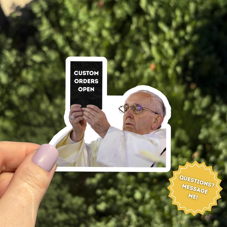 Pu&ograve; includere: Un adesivo con l'immagine di Papa Francesco che tiene in mano un cartello nero con la scritta "CUSTOM ORDERS OPEN". L'adesivo &egrave; tenuto da una mano con lo smalto viola chiaro. &Egrave; visibile anche una grafica a forma di stella gialla con la scritta "QUESTIONS? MESSAGE ME!"