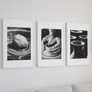 以下が含まれることがあります： 陶芸の白黒写真が3枚、額装されています。最初の写真は、ろくろの上に置かれた粘土の塊です。2枚目は、ろくろで粘土の壺を形作っている手です。3枚目は、陶器の花瓶の集まりです。