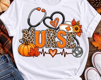 May include: A white t-shirt featuring a graphic with the word NURSE in orange and leopard print. The design includes a stethoscope, a heart, a nurse cap, a pumpkin, autumn leaves, a sunflower, and an EKG heartbeat line with a heart symbol.