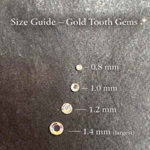 May include: A size guide for gold tooth gems. The image displays four small, round gems in different sizes: 0.8 mm, 1.0 mm, 1.2 mm, and 1.4 mm (largest). The text "Size Guide - Gold Tooth Gems" is at the top.