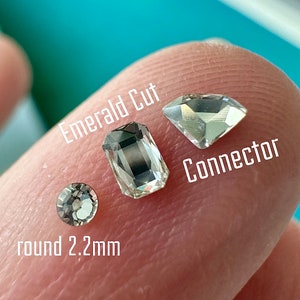 May include: Close-up of three clear, faceted gemstones: an emerald cut, a connector shape, and a round 2.2mm stone. The gemstones are displayed on a finger against a blurred turquoise background. The text "Emerald Cut", "Connector", and "round 2.2mm" are overlaid on the image.