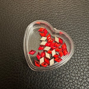 May include: A heart-shaped container filled with red and silver diamond-shaped rhinestones.