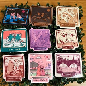 May include: A collection of nine square stickers with various cartoon illustrations and text. Designs include deer, owls, bunnies, frogs, sheep, bats, bears, and cats. Each sticker has a unique color palette and phrase, such as "Oh Deer" and "Ur Beary Special."