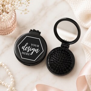 May include: Two round black compact hairbrushes with mirrors. One is closed, displaying a white hexagonal border with the text "YOUR design HERE" in the center. The other is open, revealing a circular mirror and black bristles for hair grooming.
