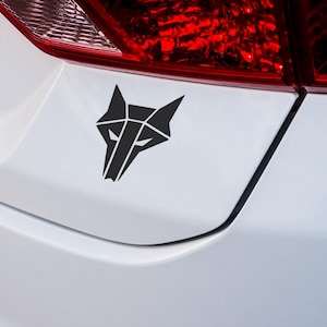 May include: A black geometric wolf head decal on a white car.