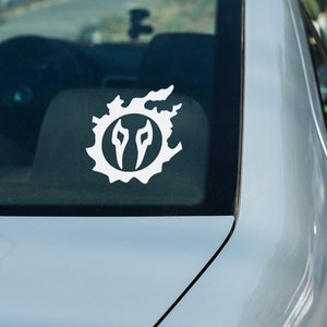 May include: A white vinyl sticker of the Final Fantasy XIV logo on the back window of a silver car.