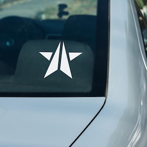May include: A white star-shaped sticker with a double line design is on the back window of a silver car.