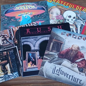 May include: A collection of classic rock vinyl record covers including Boston, The Best of Grateful Dead, Van Halen Fair Warning, Rush Moving Pictures, and Kansas Leftoverture. The album art features various illustrations, including a spaceship, a skull, a bearded man writing, and architectural scenes with bold band names.