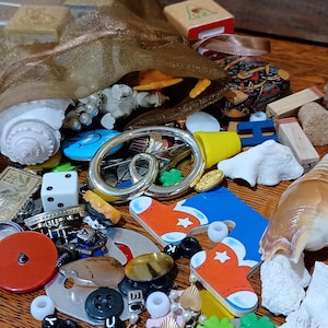 May include: A collection of assorted small objects including a gold organza drawstring bag, a white seashell, a silver pretzel-shaped pin, a red button, a blue and orange stocking-shaped cutout, dice, beads, and various small trinkets.
