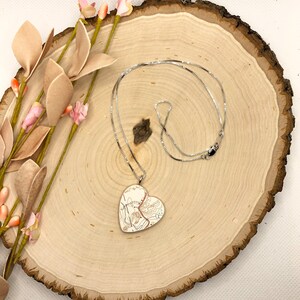 May include: A silver chain necklace with a heart-shaped pendant. The pendant is made of white metal and features a detailed map design.