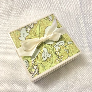 May include: Set of four square coasters featuring a vintage map of a lake with multiple ponds. The coasters are tied together with a white ribbon.