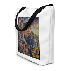 May include: White tote bag with black straps. The bag displays a colourful painting of people and a mountain scene. A figure in a military uniform is visible, along with the gold numbers "50 1976-2026".