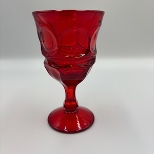 May include: A ruby red vintage goblet with a textured design. The glass features a rounded bowl, a slender stem, and a circular base. The goblet is made of a transparent, glossy material.