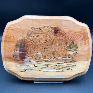 May include: A wooden serving tray with a carved relief of two bears. The bears are depicted in a naturalistic style, with detailed fur and facial features. The tray has a light brown color and a unique, irregular shape.