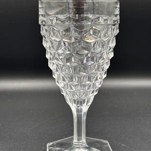 May include: Clear, faceted glass goblet with a hexagonal base and a stem. The bowl of the glass has a geometric, cube-like pattern. The glass is transparent, allowing light to pass through. The goblet is likely for serving beverages.