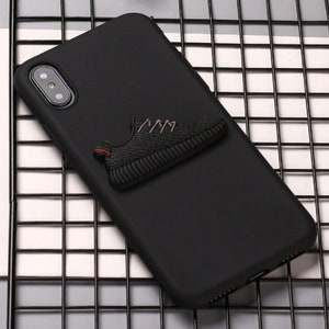 Puede incluir: Funda de tel&eacute;fono negra con una zapatilla negra 3D unida a la parte posterior.